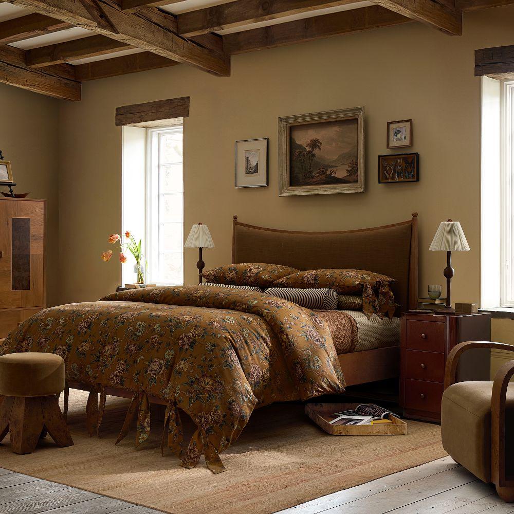 Warm bedroom with wooden beams, patterned bedding, brown leather headboard, and traditional furnishings