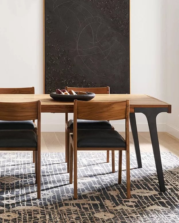 Mid-century wooden dining table with black leather chairs and a large blackboard wall behind
