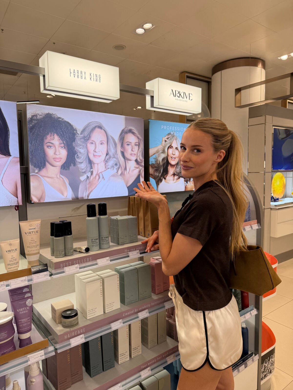 Woman in black shirt and white shorts standing in a hair care retail store with product displays and brand signage