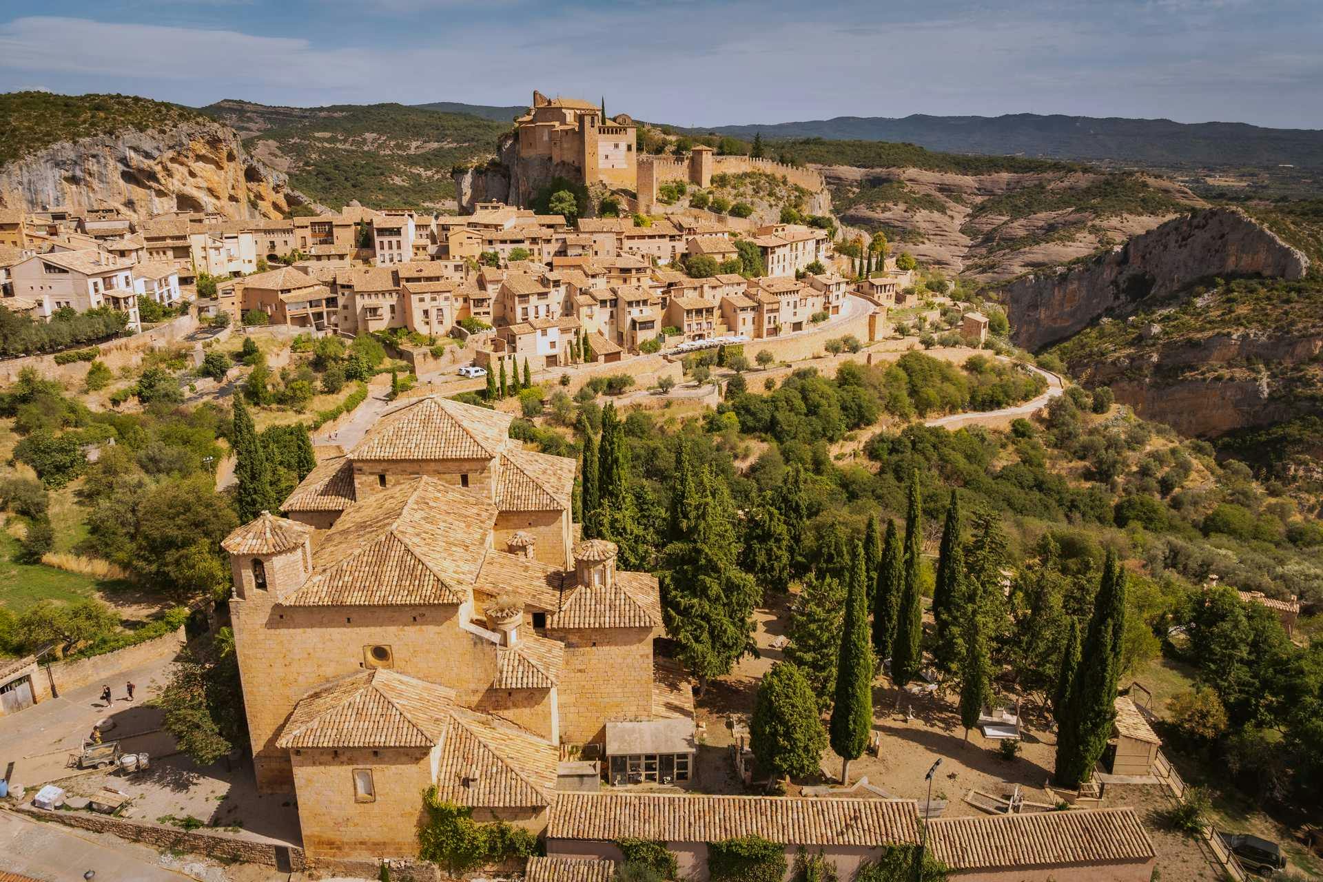 Aerial view of hilltop village with terracotta-roofed buildings, castle, and surrounding forested landscape