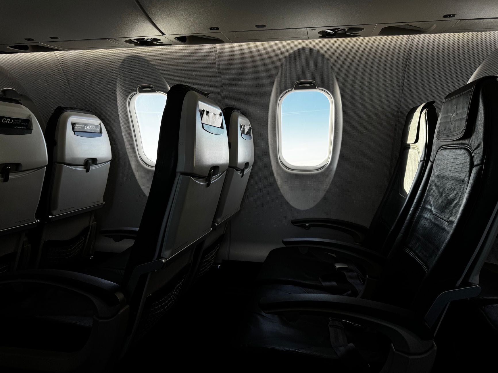 Aircraft cabin interior with empty black seats and oval window showing blue sky outside