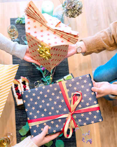 Hands exchanging wrapped gift boxes with star patterns and colorful ribbons on wooden floor