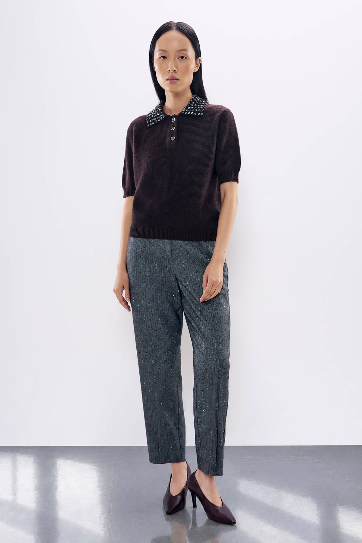 Woman in burgundy polo sweater with studded collar and gray sparkly trousers