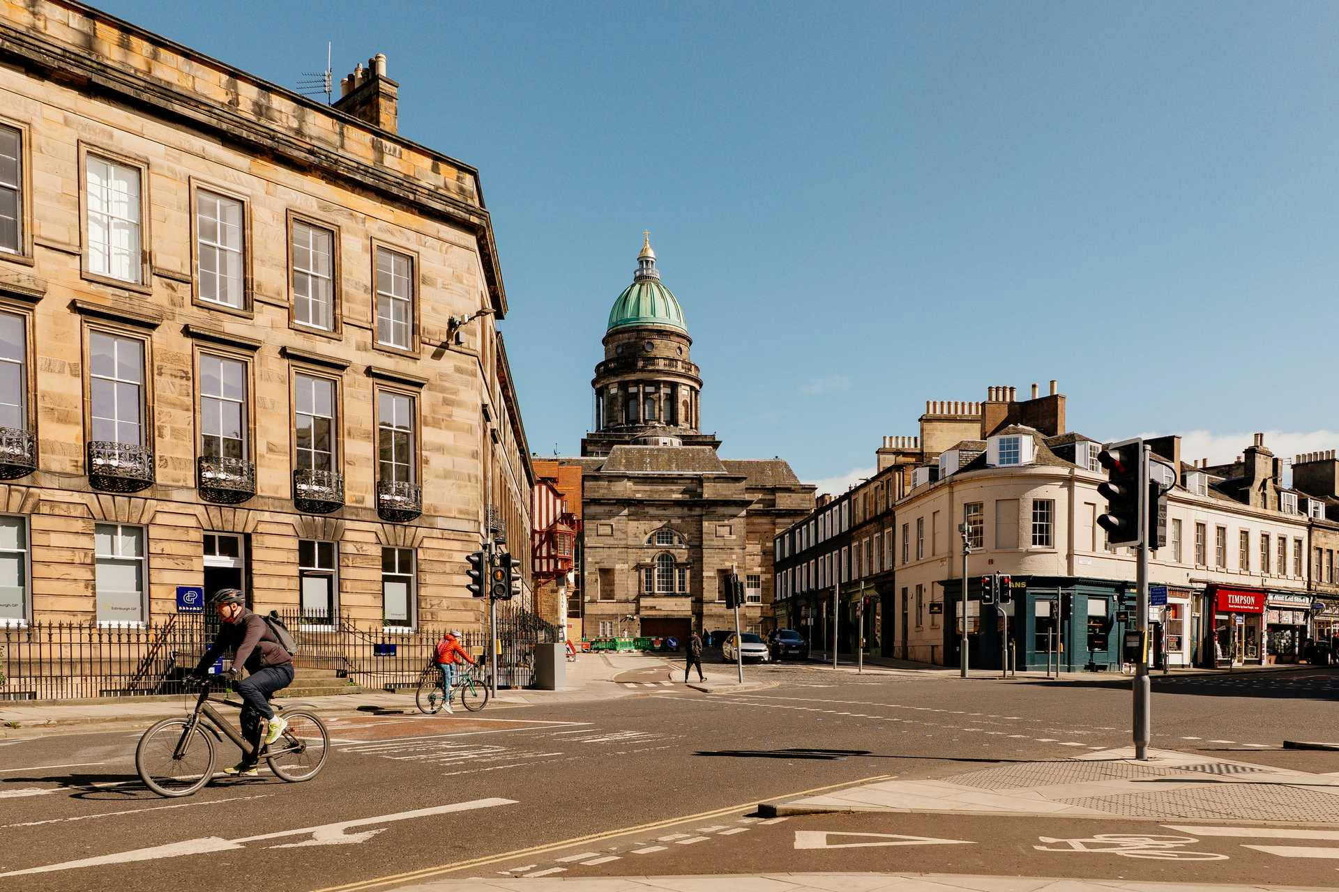 Scottish city street with historic stone buildings, cyclists, and domed church with green dome