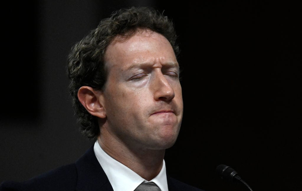 Man in dark suit and tie with eyes closed, photographed in profile against black background