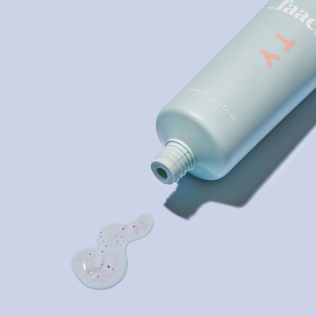 Light blue cosmetic bottle with coral text dispensing white gel product