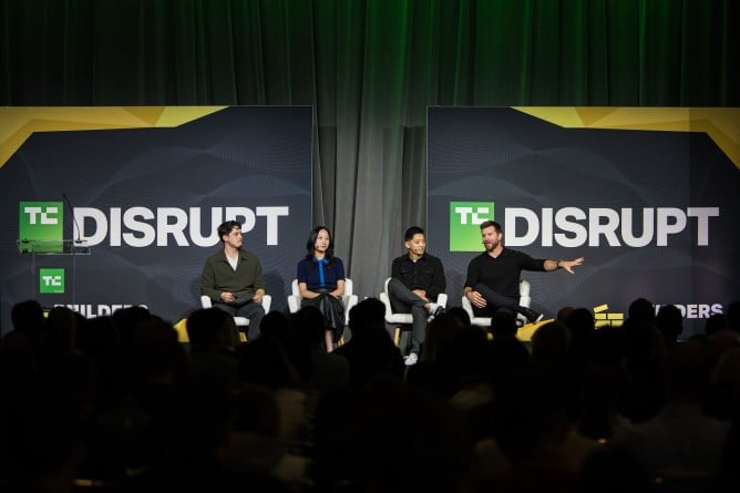 Four panelists sitting on stage at a tech conference with audience silhouettes in foreground