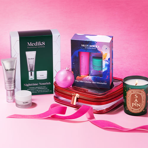 Nighttime nourish skincare set with green packaging, pink cosmetic bag, and scented candle on pink background