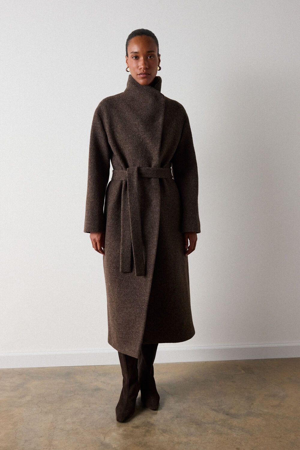 Woman with short dark hair wearing brown turtleneck wrap coat with belt over dark tights