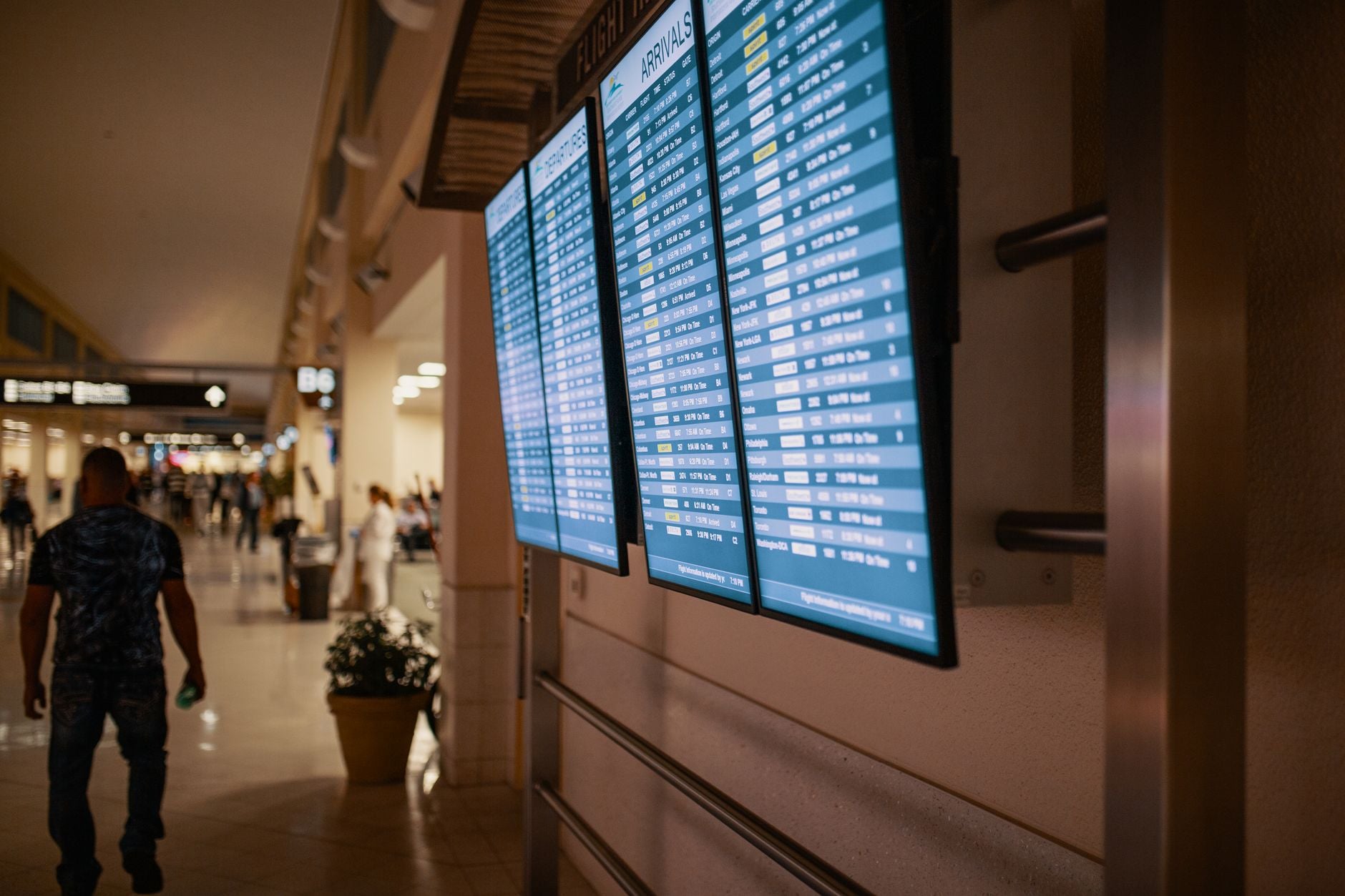 Arrivals information display screens mounted on terminal wall with blurred passengers walking below