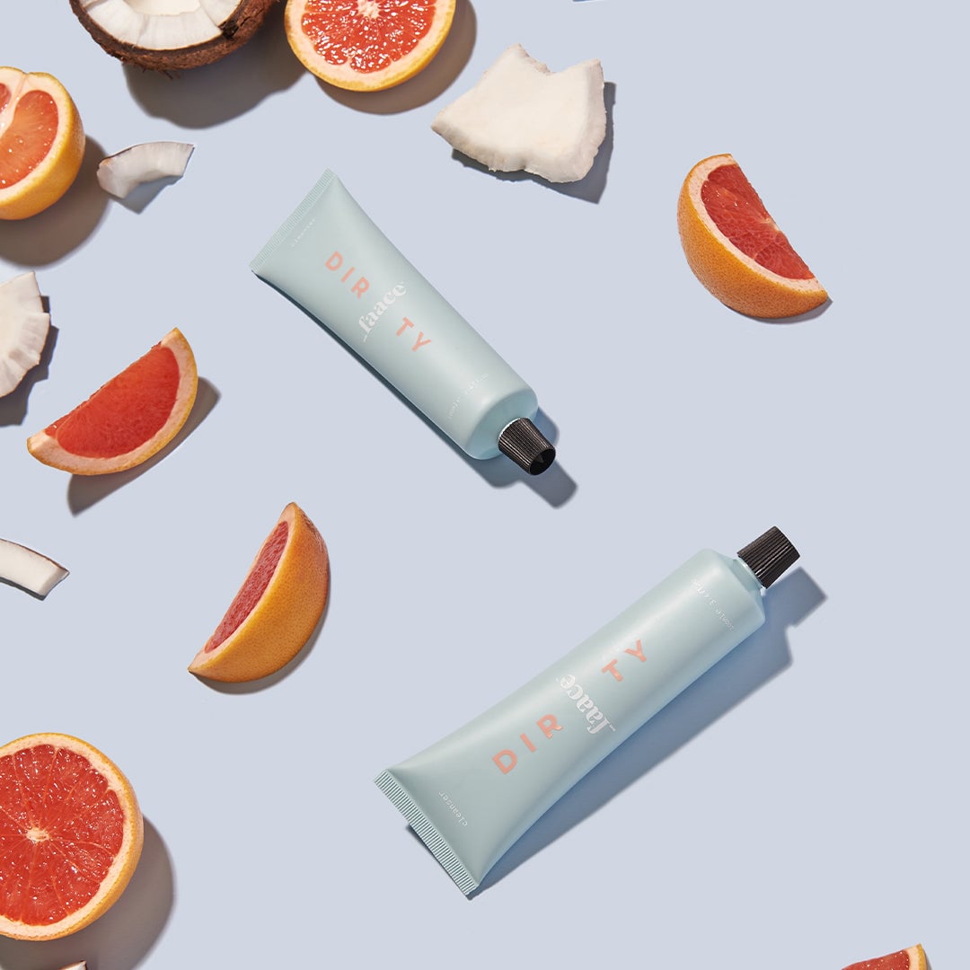 Two skincare tubes surrounded by grapefruit and coconut halves on blue background