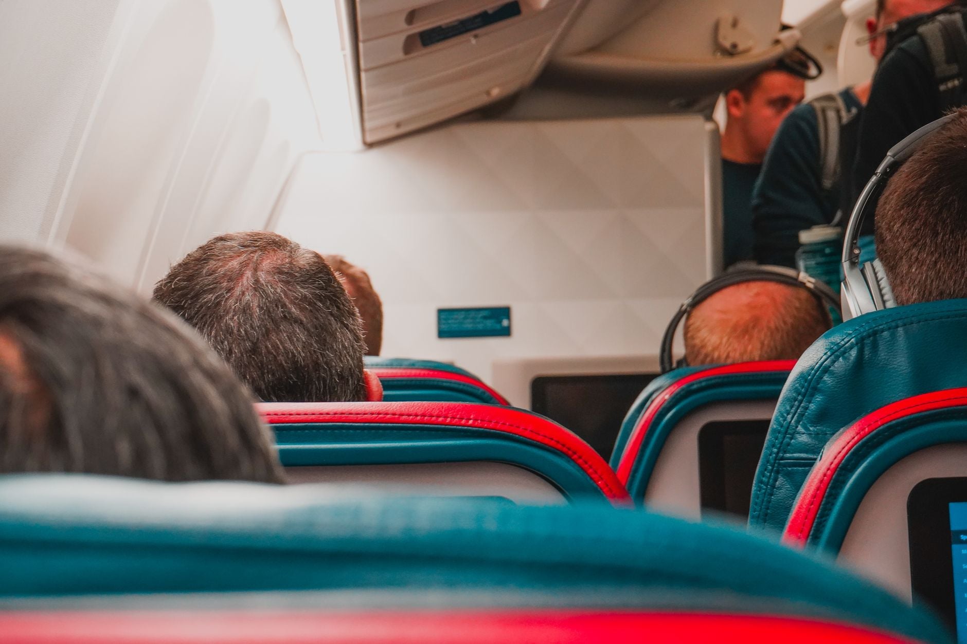 Passengers seated in airplane cabin with teal and red seat covers during flight