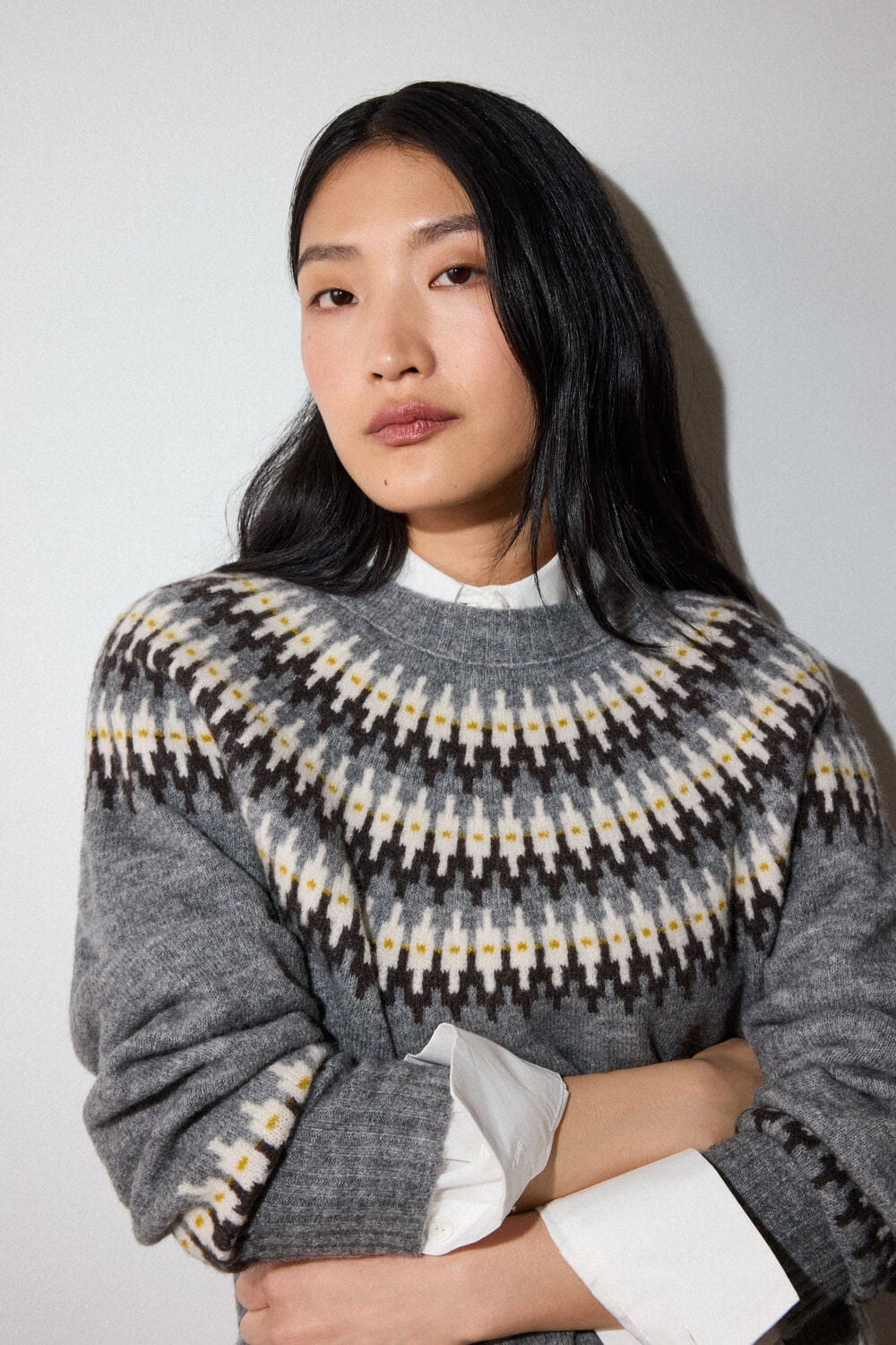 Woman with long black hair wearing gray sweater with geometric patterned yoke and white undershirt