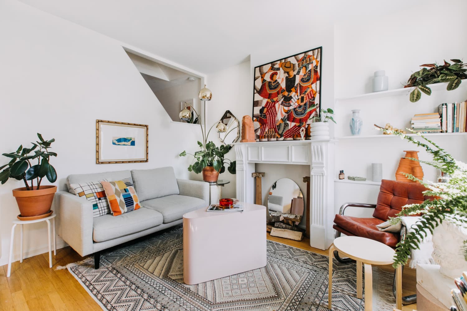 Bright living room with gray sofa, colorful pillows, potted plants, white shelving, and fireplace