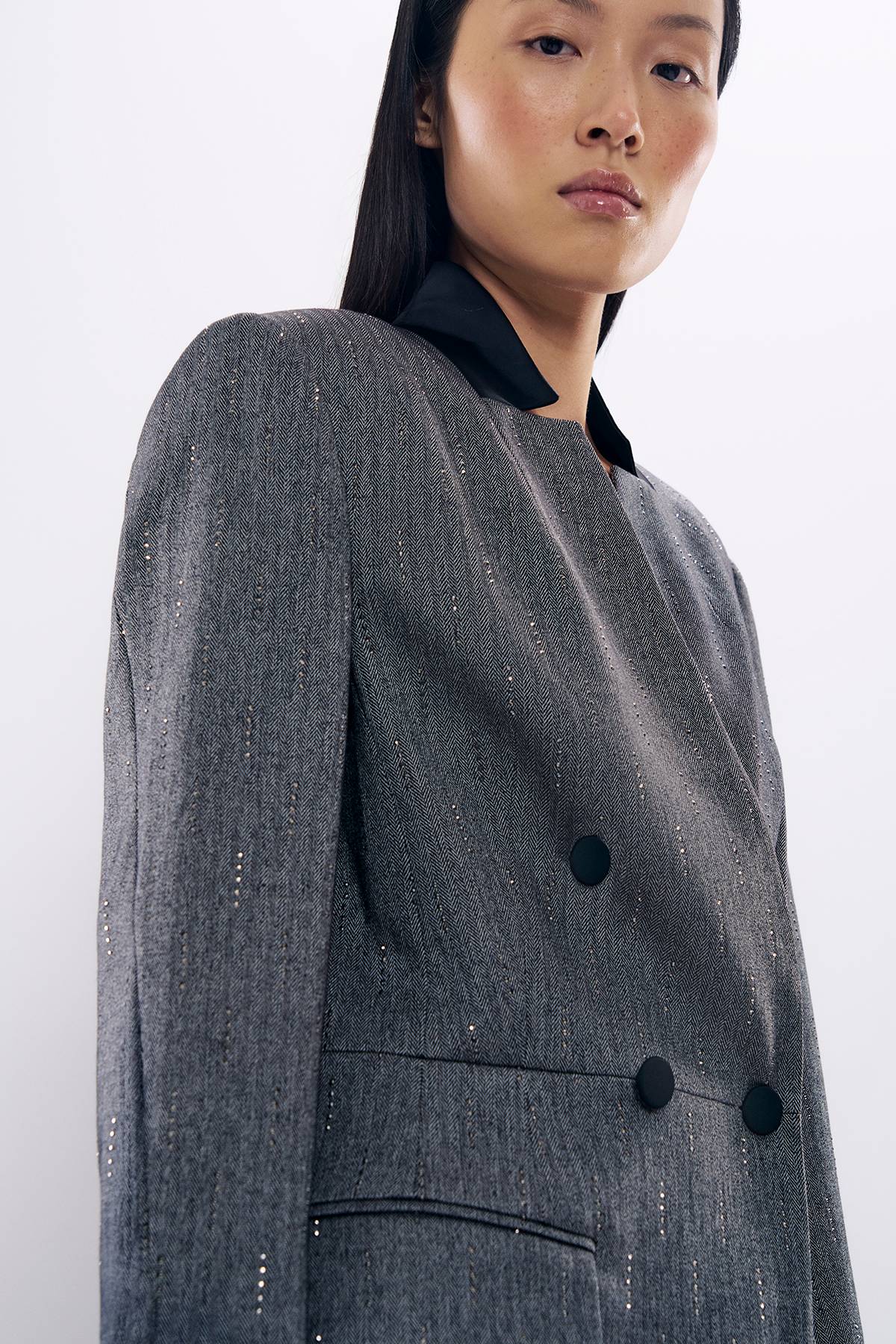 Woman in gray double-breasted blazer with sparkly embellishments, looking over shoulder