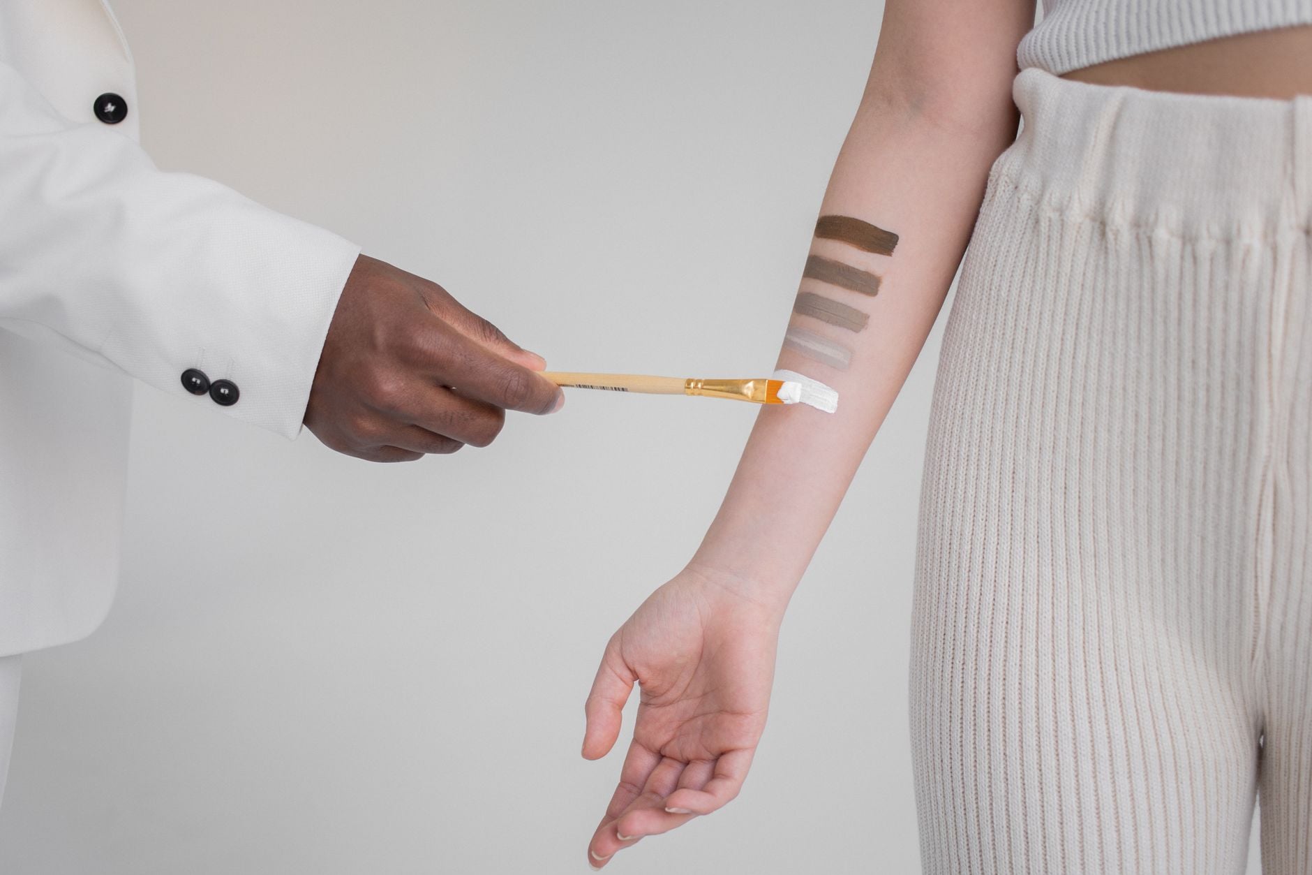 Person demonstrating concealer swatches on arm with brush applicator showing various shade coverage levels