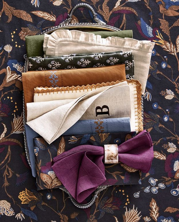 Decorative fabrics and linens arranged in a basket, including patterned and solid textiles in jewel tones