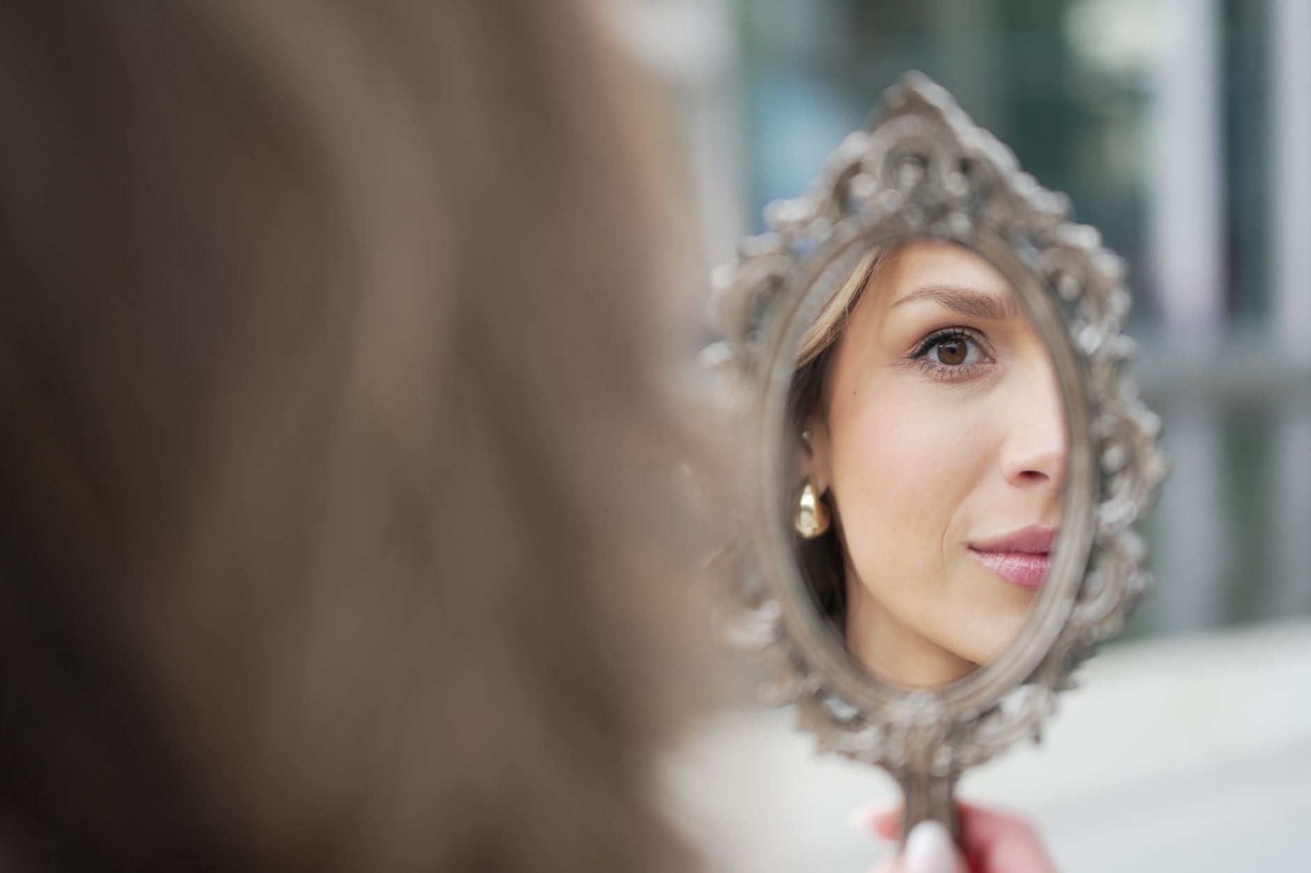 Woman with gray hair looking at her reflection in an ornate decorative mirror