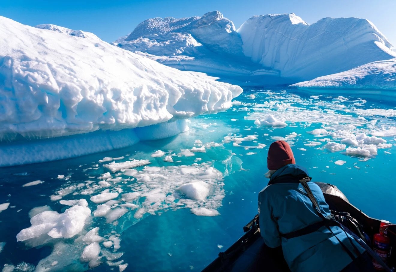 Kayaker approaching large white icebergs floating in bright turquoise water surrounded by snow-covered peaks