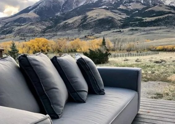 Gray outdoor daybed with dark pillows overlooking mountain landscape and golden fields