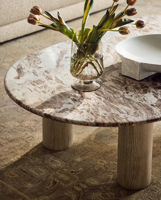 Round marble-top side table with wooden pedestal base holding a glass vase with burgundy tulips