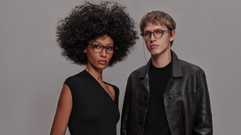 Two people wearing eyeglasses posing against neutral gray background