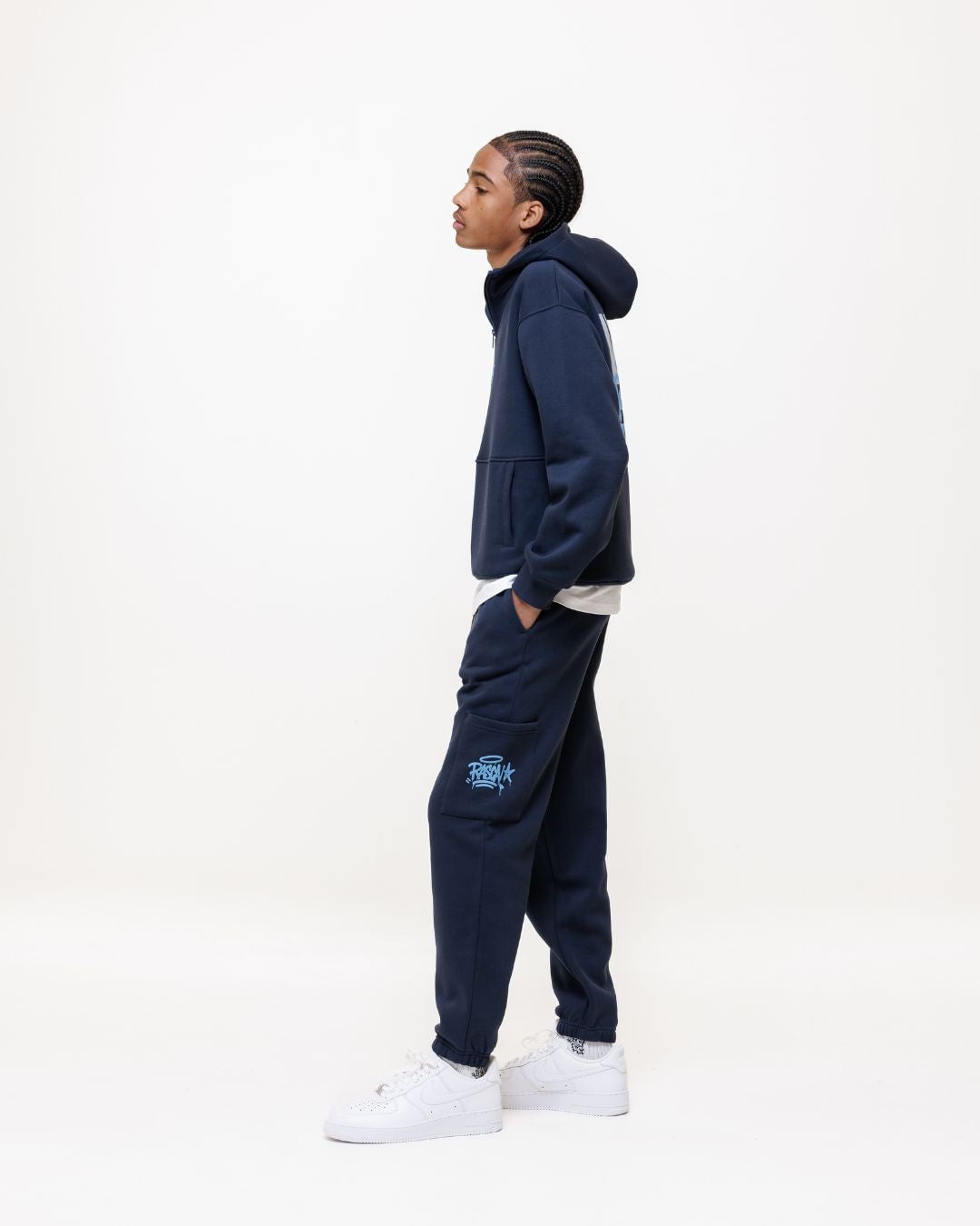 Person standing in profile wearing navy hoodie and matching navy cargo pants with white sneakers